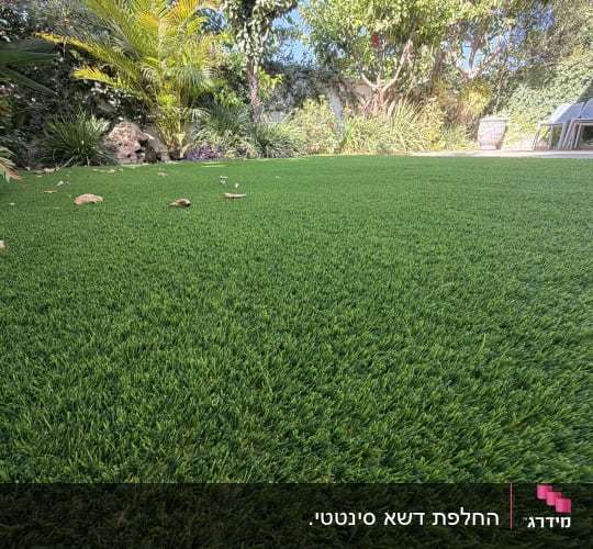 מדשאת דשא סינטטי מותקנת בגינה פרטית עם צמחייה ועצים ברקע